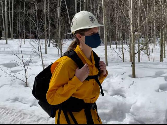 Woman in hard hat walks through snowy forest