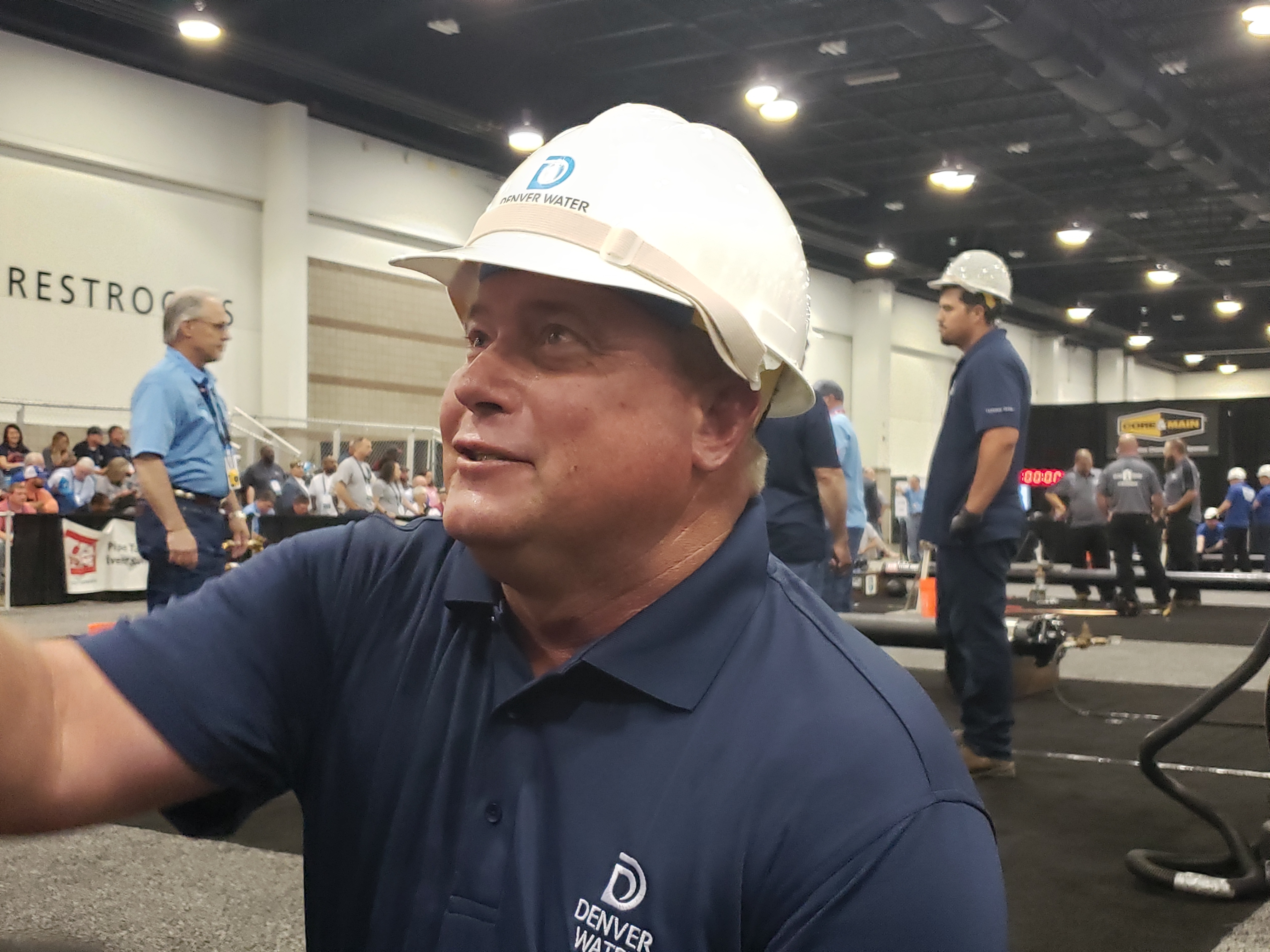 A man in a Denver Water hard hat smiles at friends in an exhibit hall.