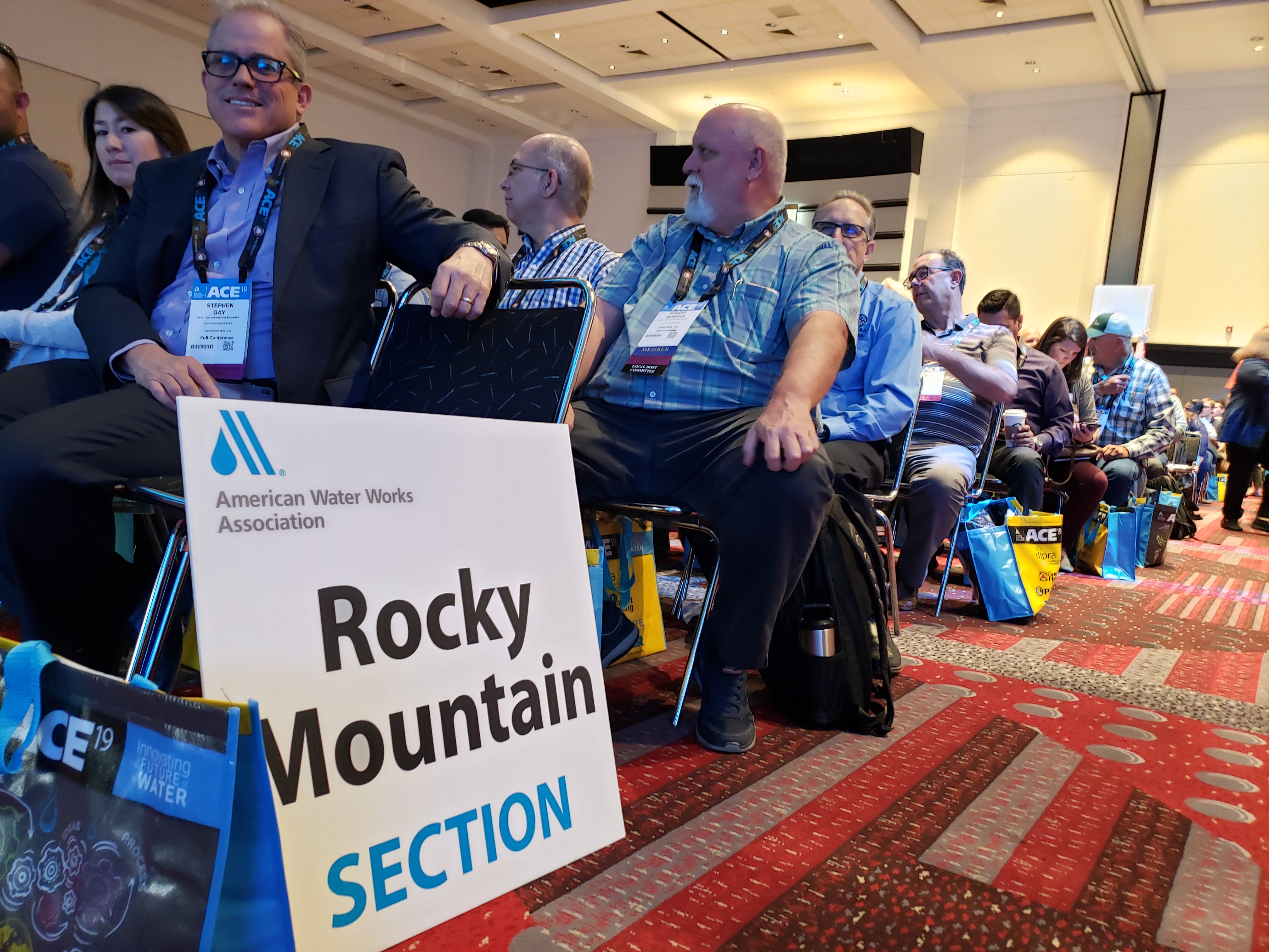 A sign for the Rocky Mountain section sits on the ground in a crowded ballroom.