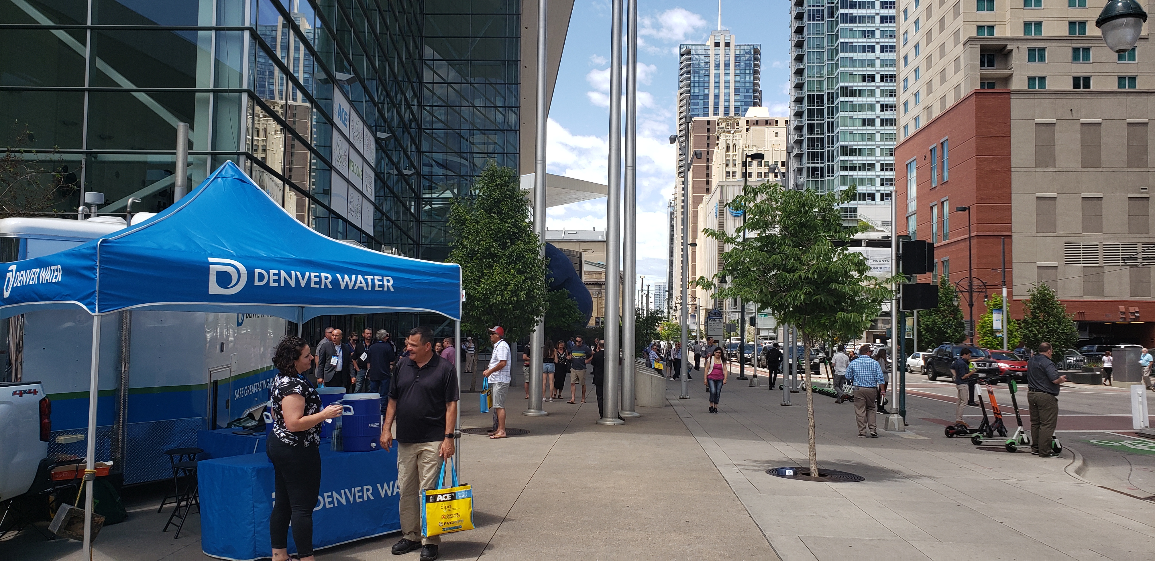 A Denver Water tent on the sidewalk of a busy city street.