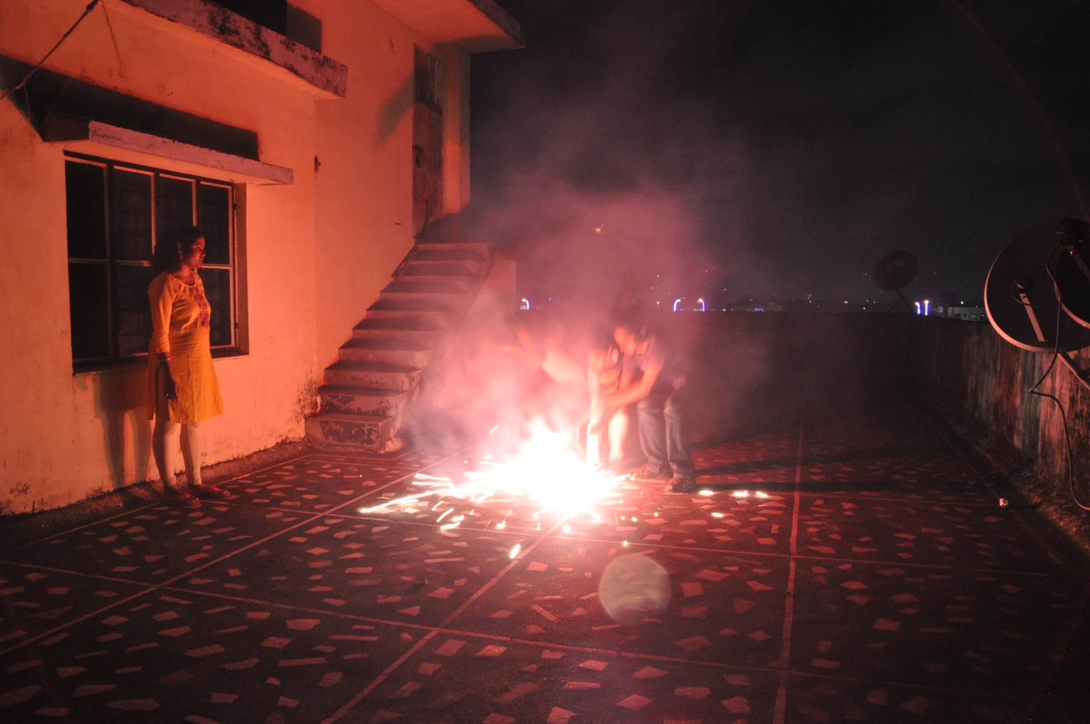 Children are seen lighting fireworks on a patio with the city lights in the background.
