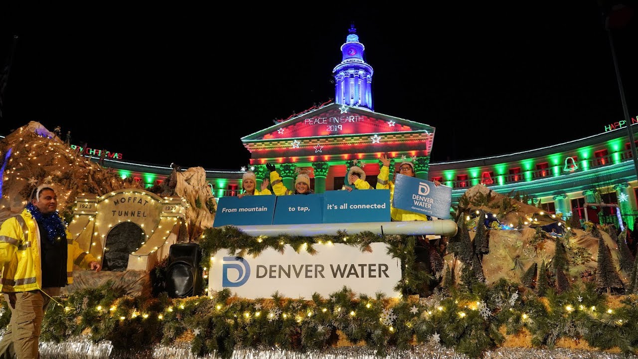 Kidgs wave from atop a float under the Denver City and County building that's lit for the holiday season.