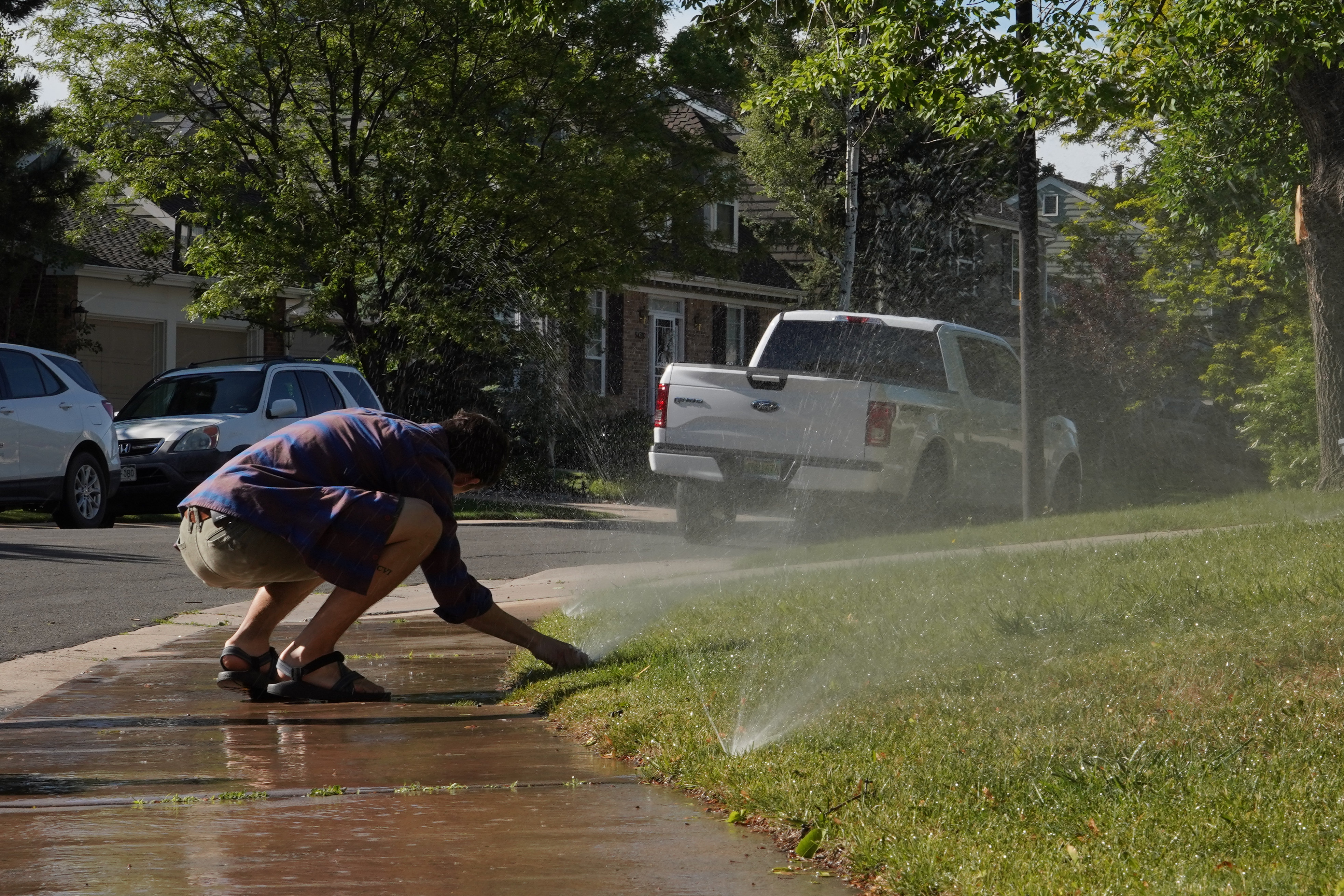 This picture shows a technician adjusting a sprinkler head so that water sprays onto the yard and not the sidewalk.