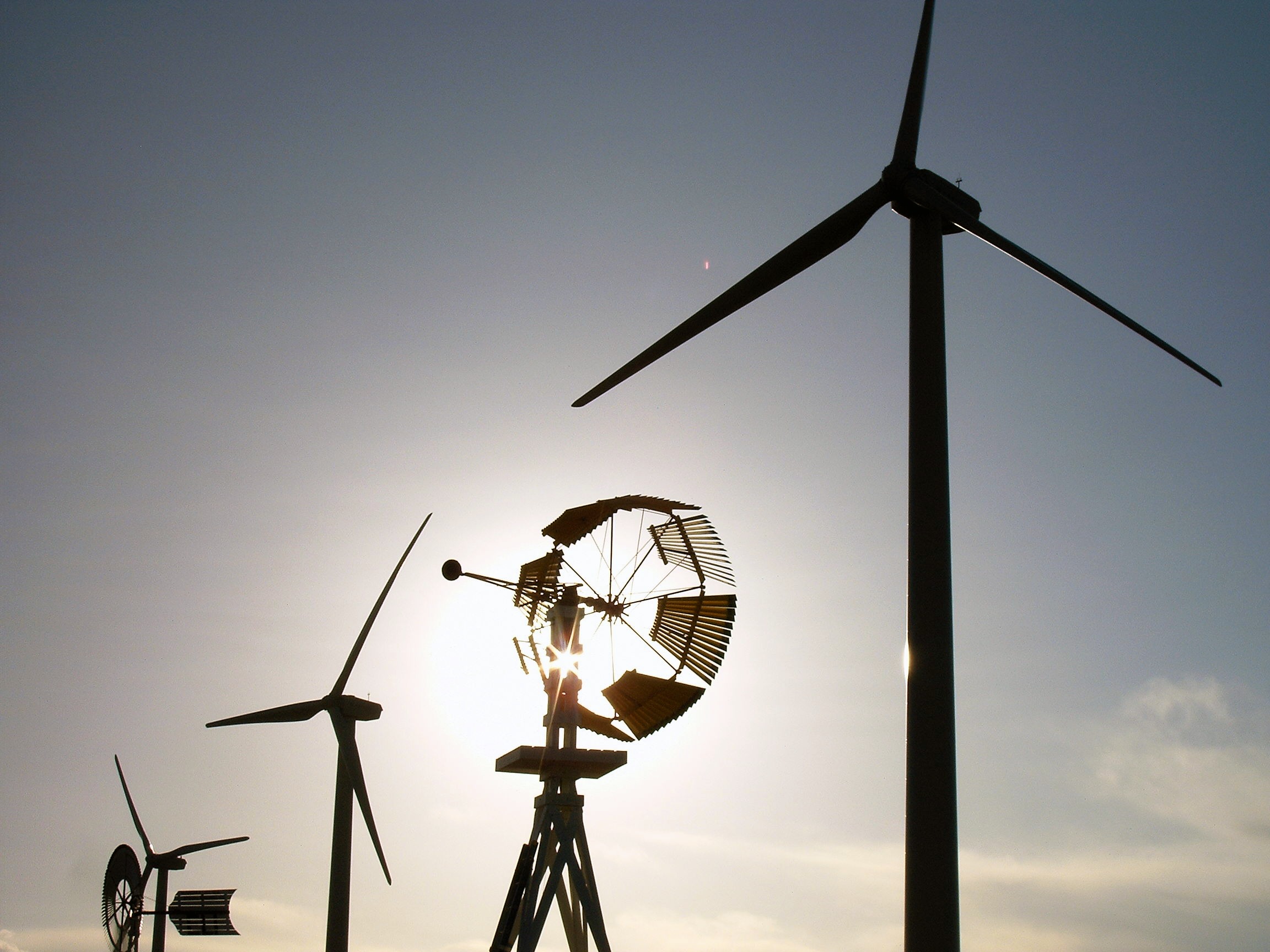Modern-day wind turbines are mixed with old-school windmills, all silhouetted against the sky.