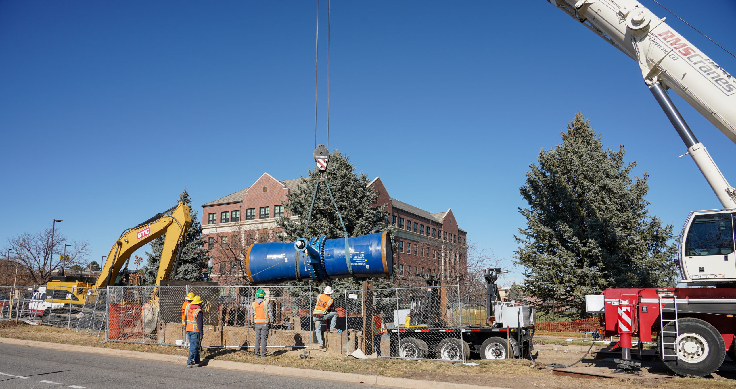 Construction workers lower a large valve into a trench at West 50th Avenue and Irving Street in front of Regis University. Photo credit: Denver Water.
