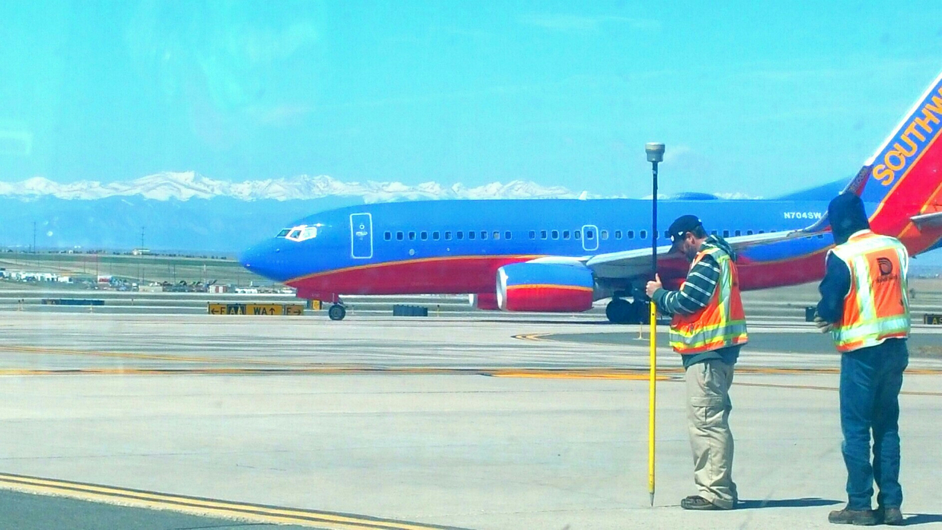 Denver Water survey crew working on a runway at Denver International Airport with a view of a Southwest Airlines jet and the snow-capped Rocky Mountains behind them.