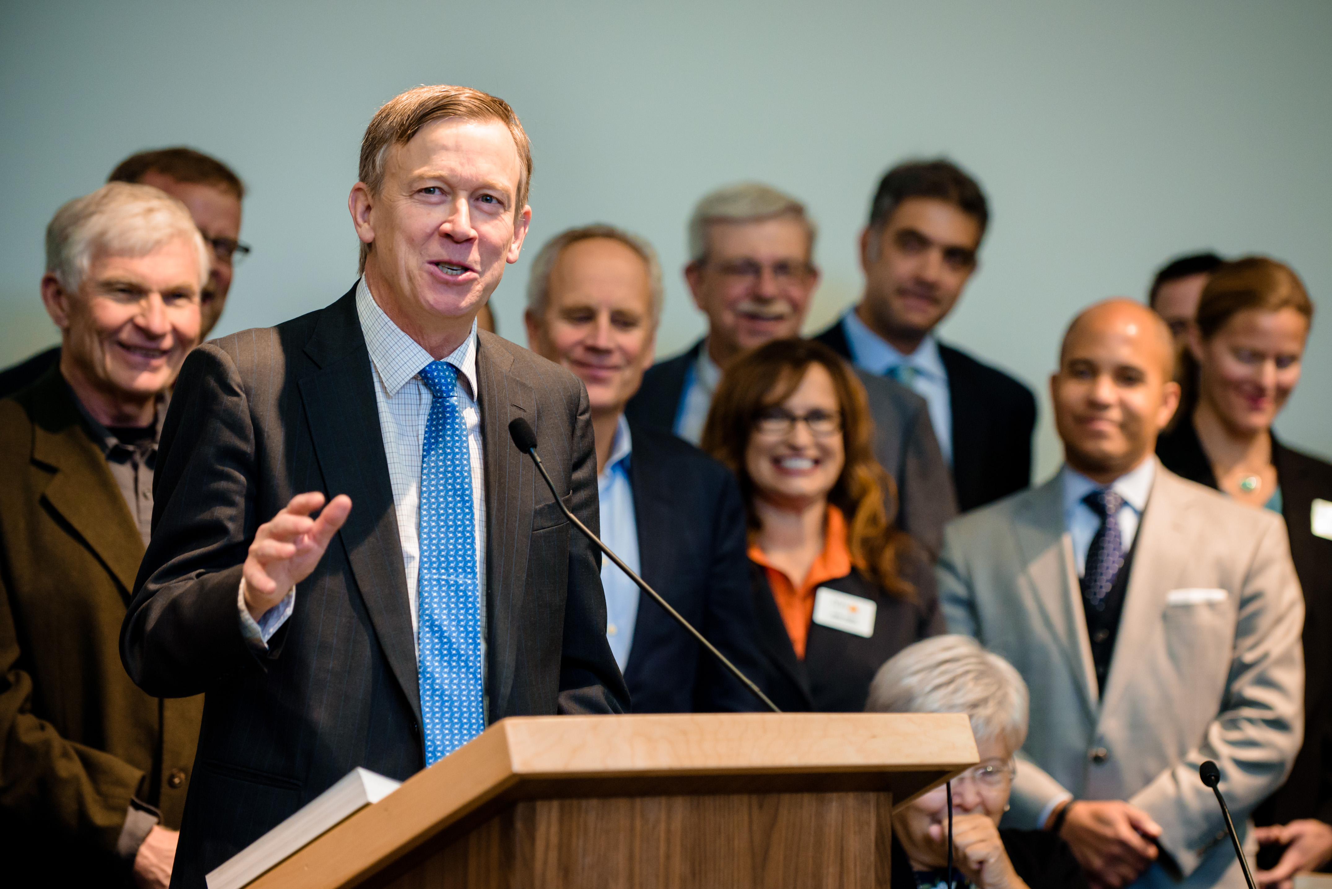 Colorado Gov. John Hickenlooper standing at a podium surrounded by smiling people.