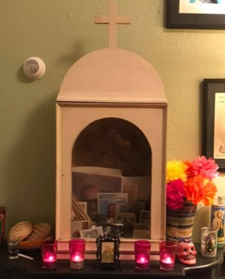A wooden box sits on a mantel, through the front opening you can see pictures. In front are four lit candles.