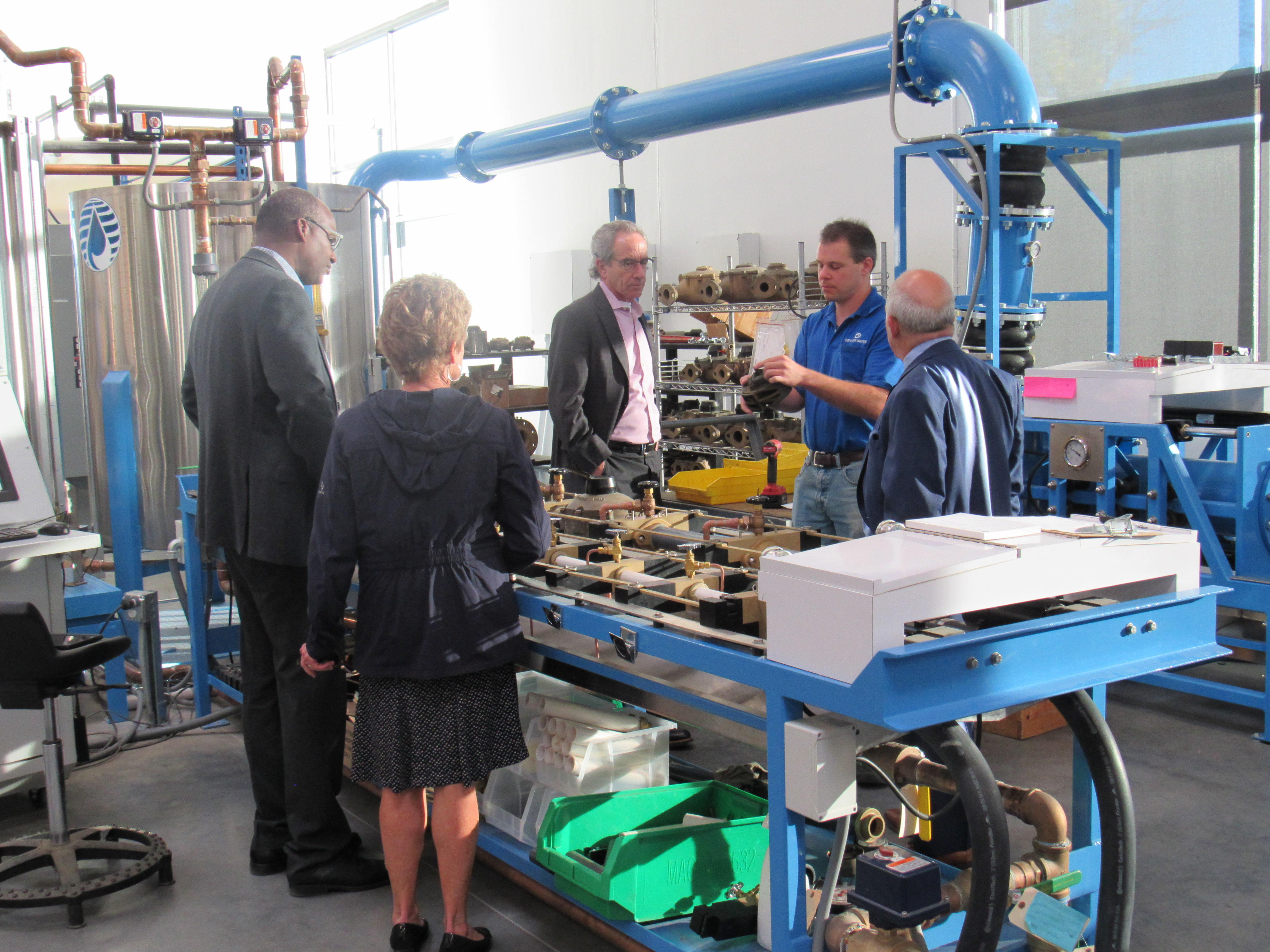 A group of people stands around a set of equipment used for testing meters.