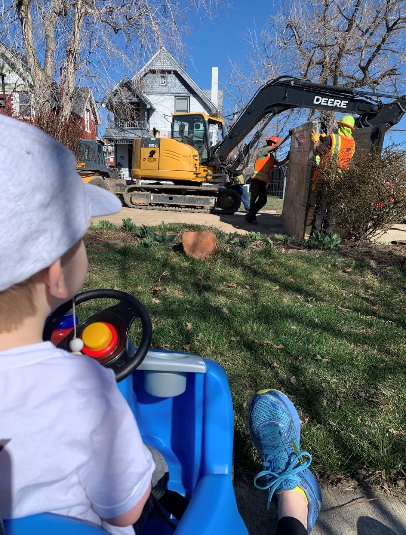 A boy watches workmen and a digging machine.