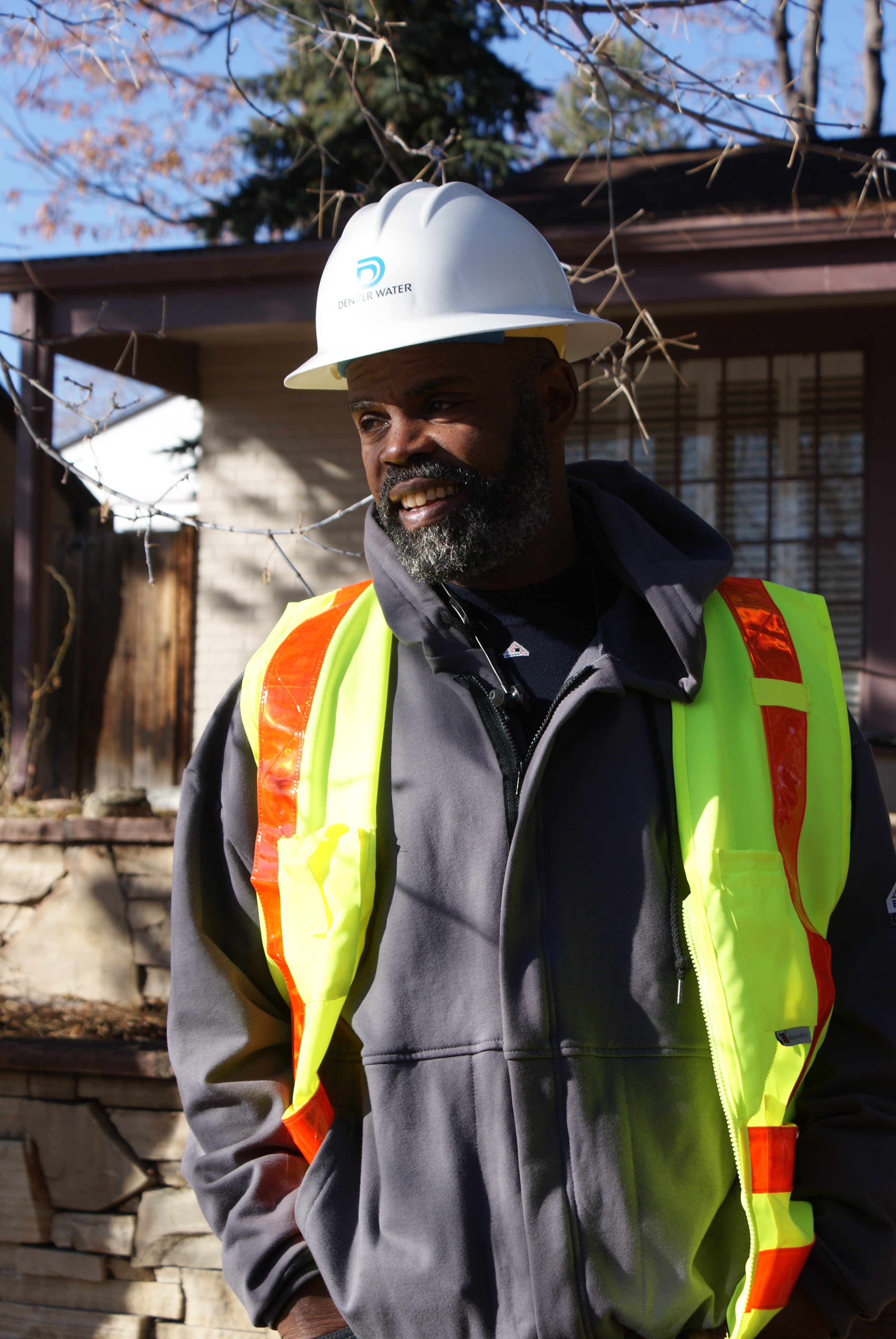 A man in a Denver Water hardhat smiles at something off camera.