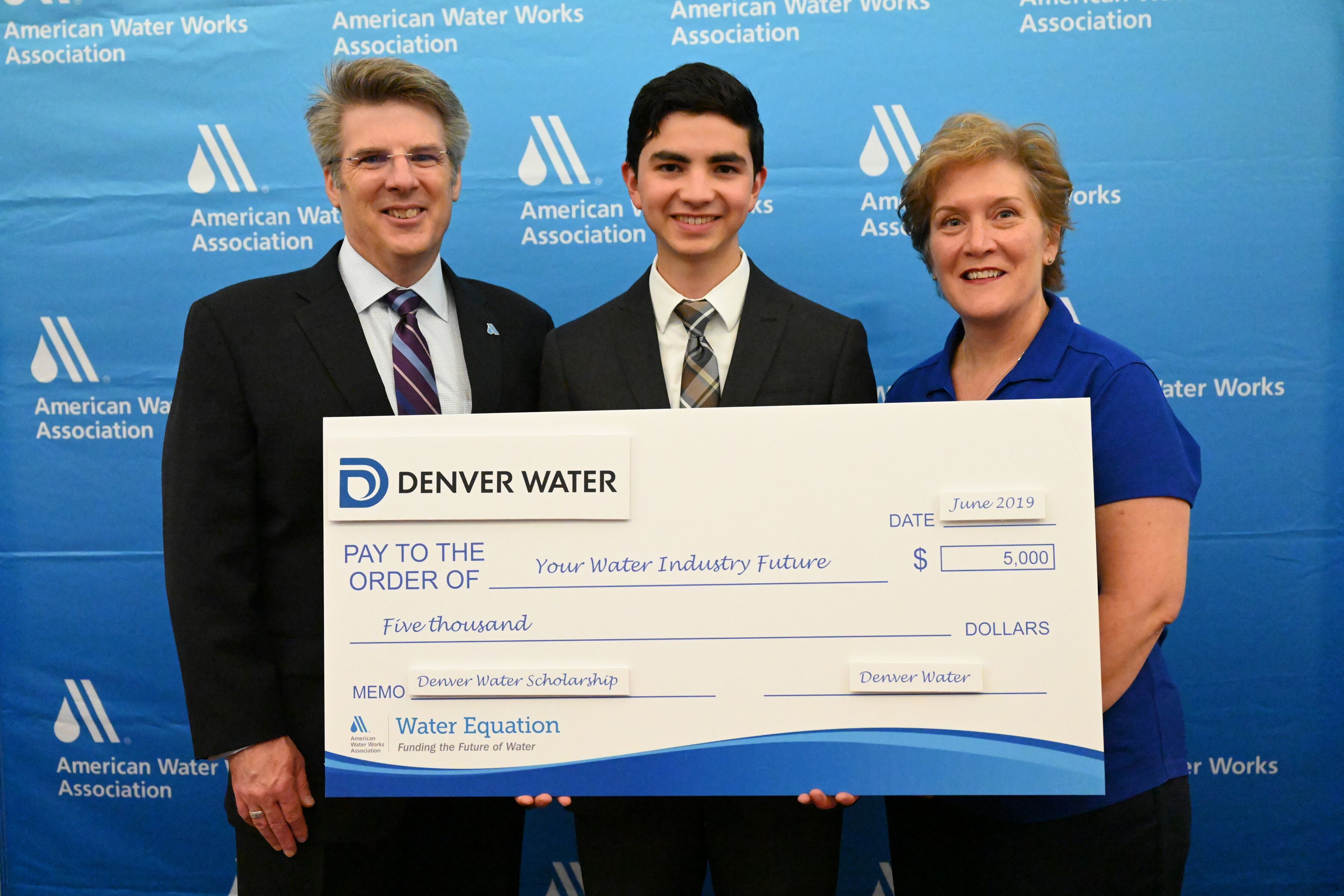 Three people stand holding a giant check for $5,000 made out to "Your Water Industry Future" from Denver Water.