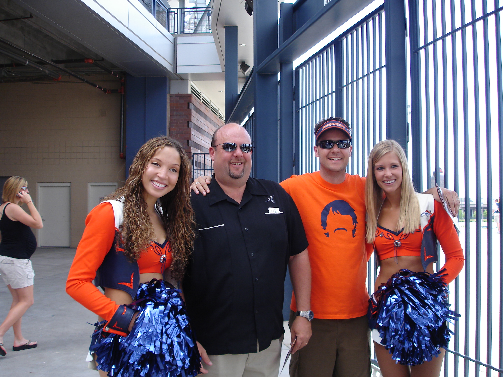 Two men in Denver Broncos fan shirts smile for the camera with two DEnver Broncos cheerleaders.