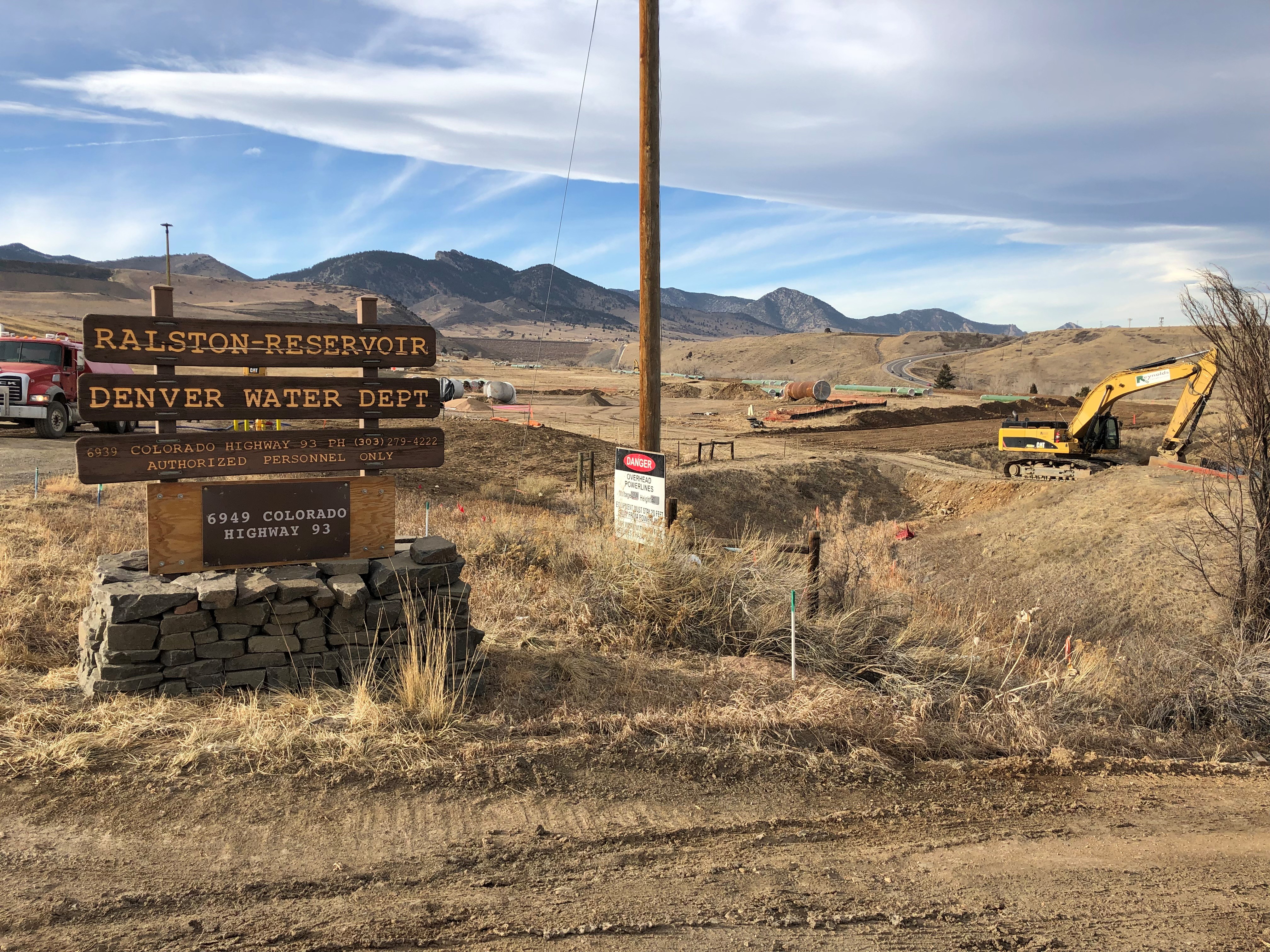 A sign says "Ralston Reservoir, Denver WAter Dept" and in the distance is construction equipment, foothills and white clouds in a blue sky.