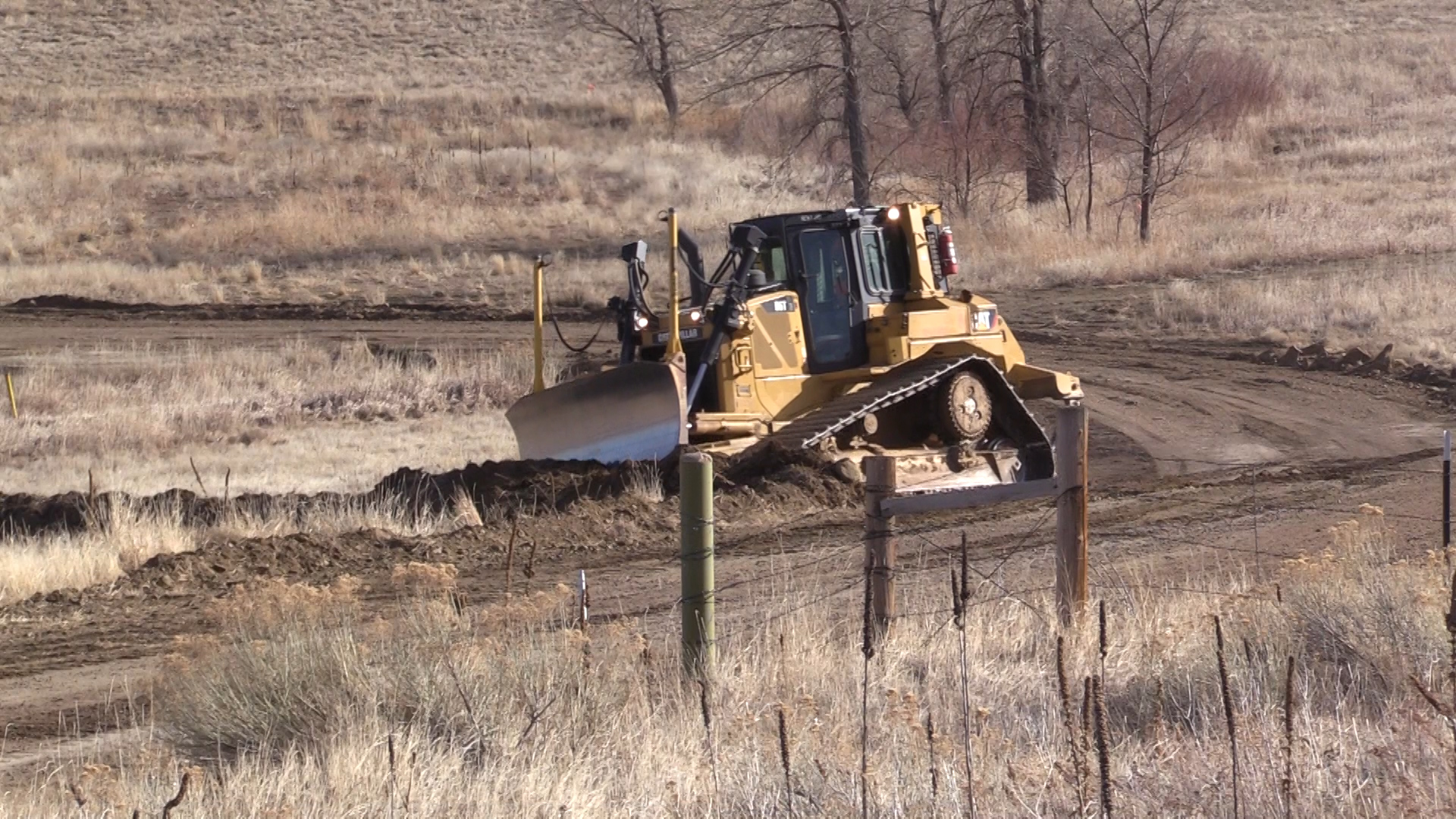 A bulldozer pushes dirt to create a road through dry grass.