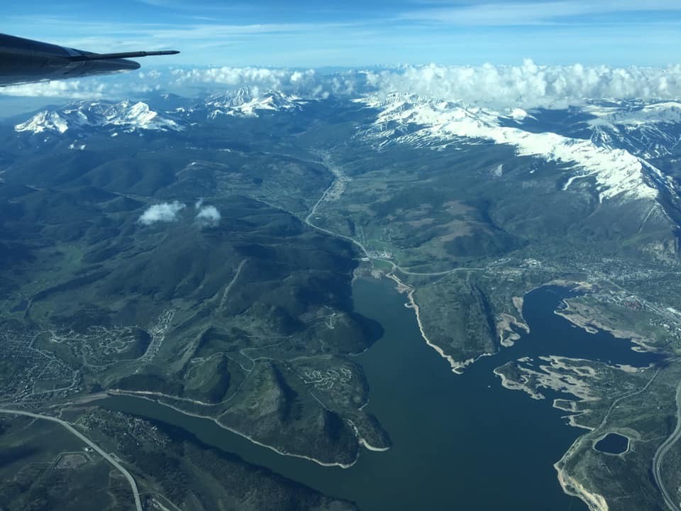 The wingtip of a plane can be seen in the upper right of the image, with Dillon Reservoir and snow-capped peaks below.