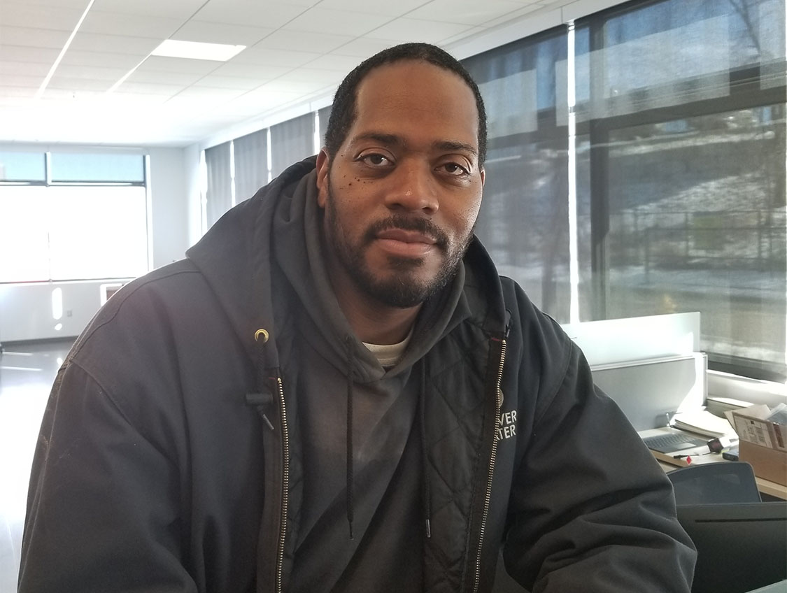 Marcus Porter, wearing a sweatshirt with a Denver Water logo, smiles for the camera in an office.