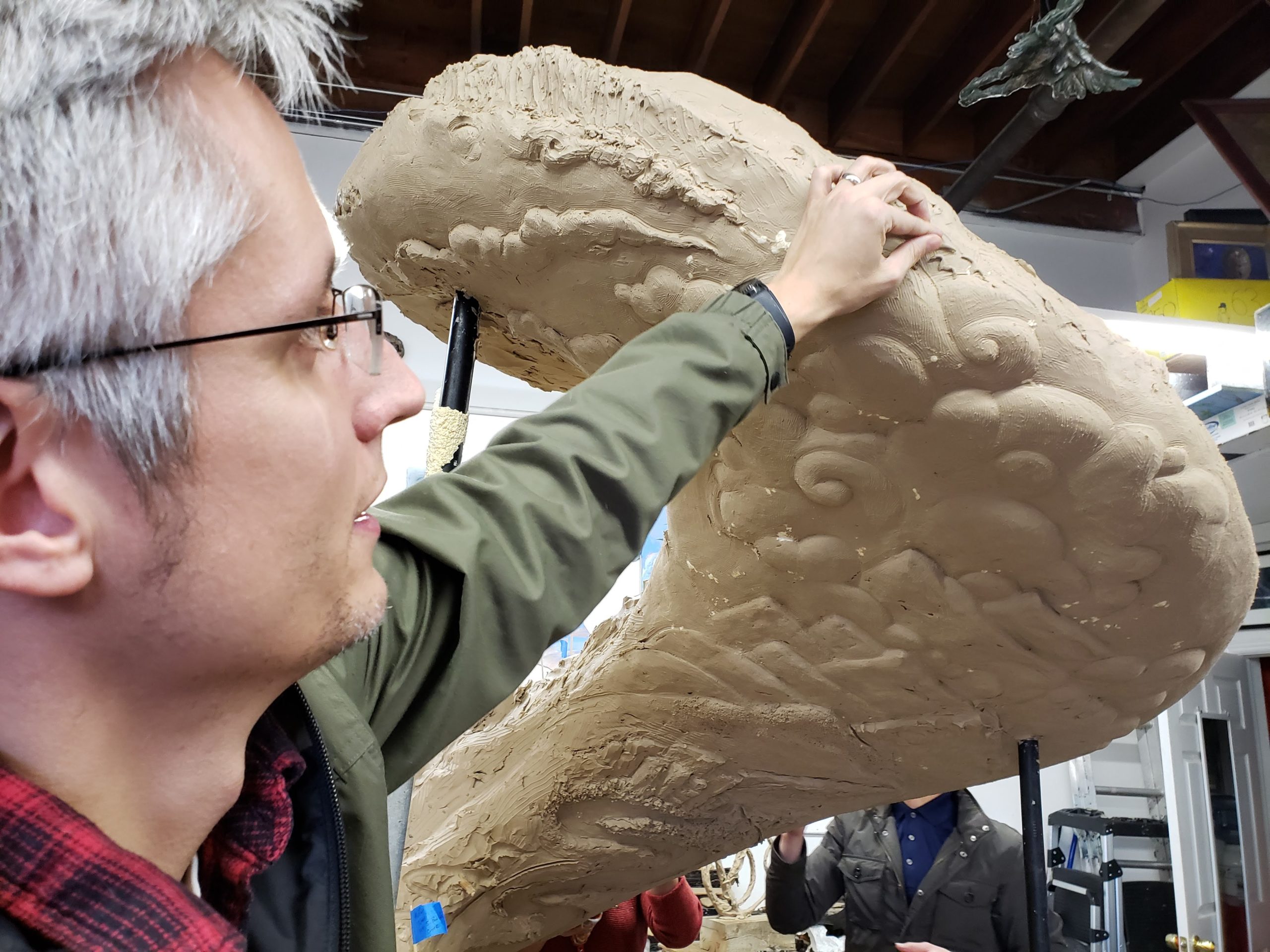 A man, arm raised high, presses a small clay bird into a massive clay sculpture.