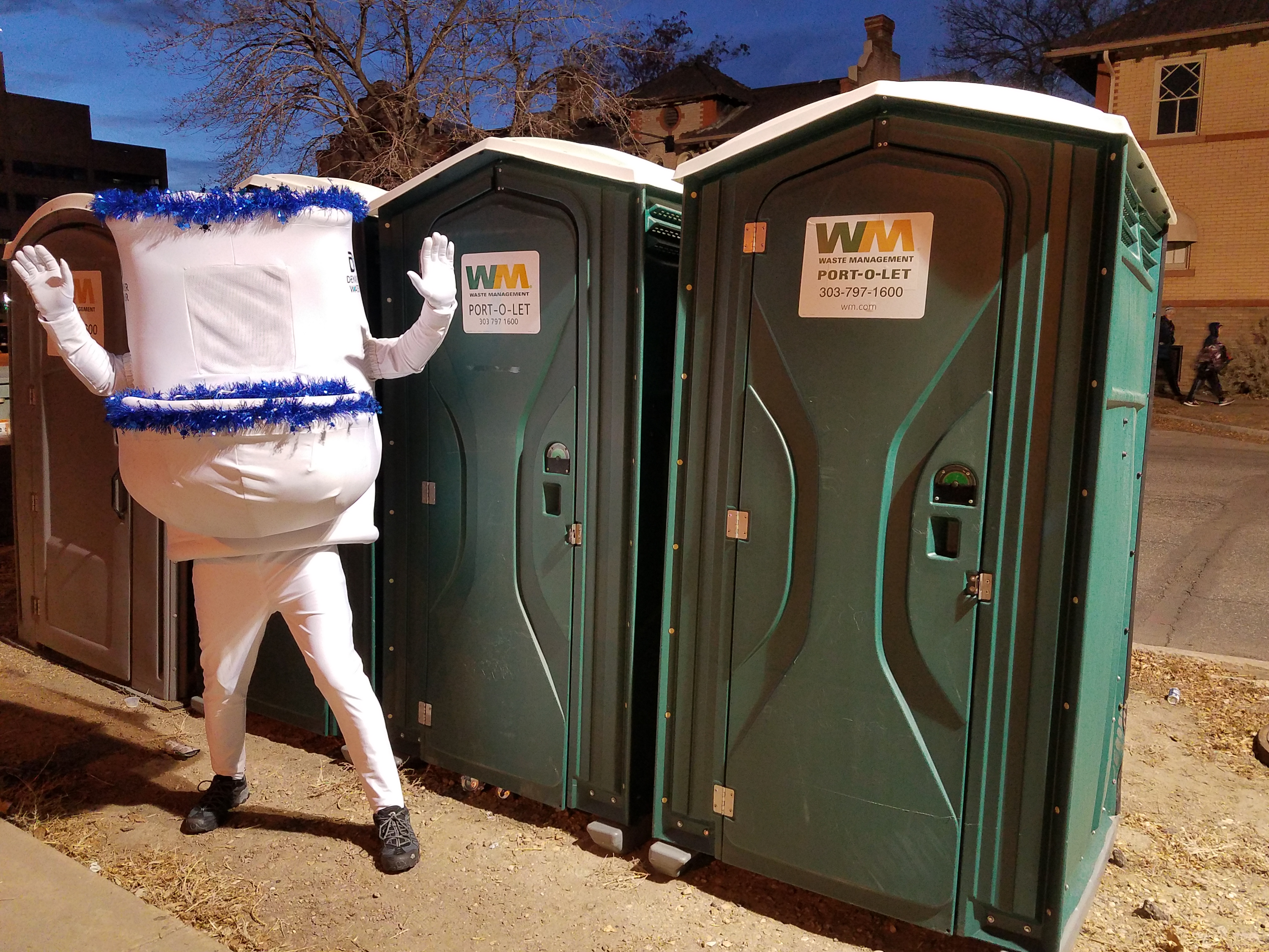 Denver Water's "running toilet," with blue garland around the top of the tank and the bowl, stands in front of a row of portable toilets.