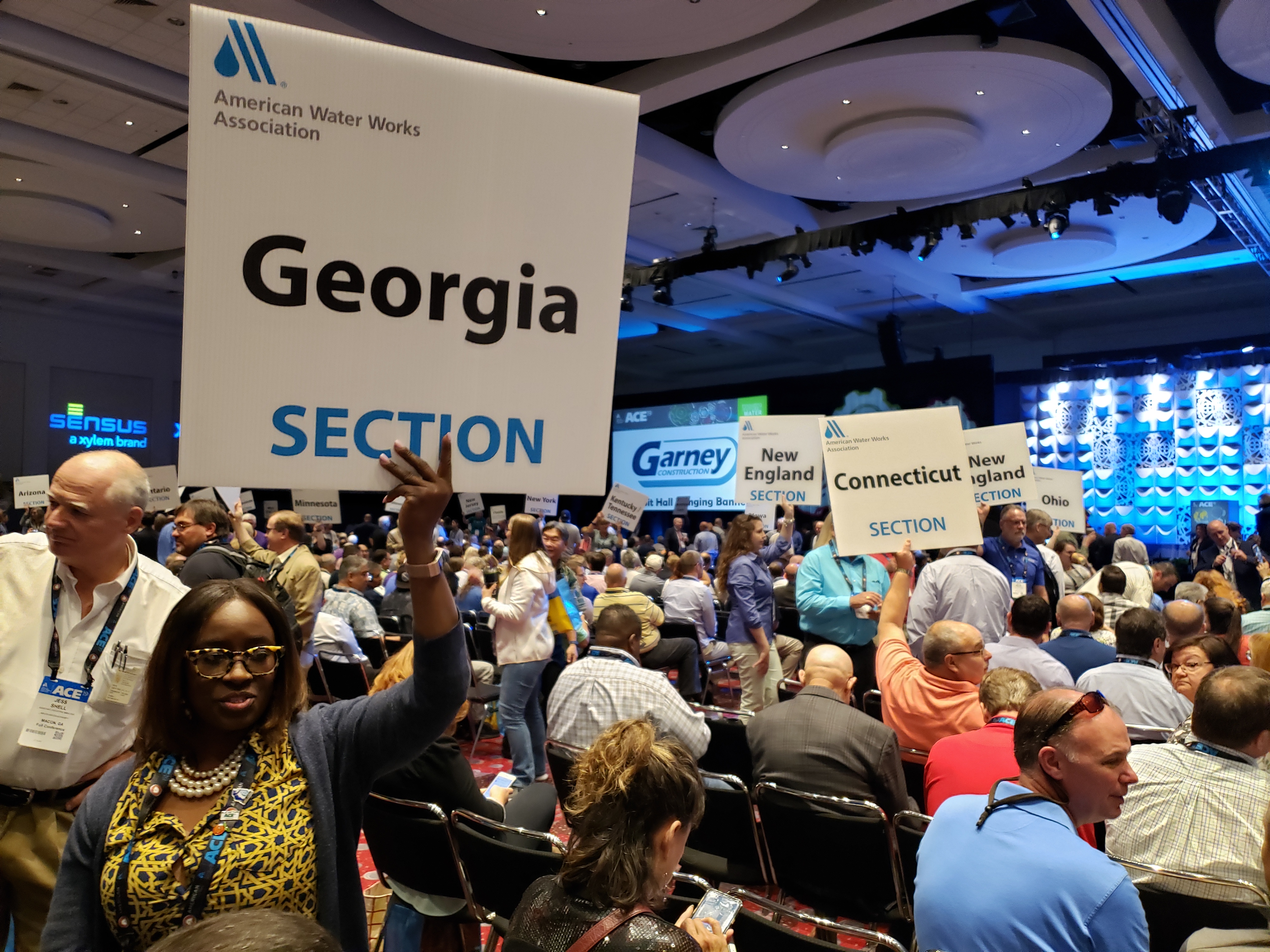 Signs for the Georgia, New England, Connecticut and Ohio sections of the American WAter Works Association can be seen in a crowded ballroom.